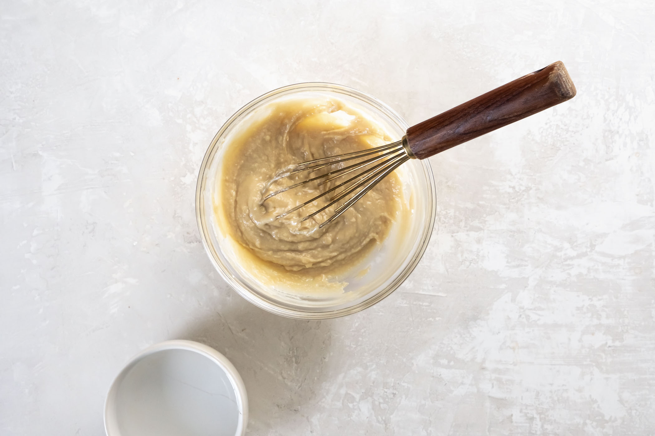 Best easy homemade Tahini Sauce recipe! This Middle Eastern sauce is made with tahini (sesame seed paste), garlic and lemon juice. It's creamy, tangy and bright, with a slight nutty flavor. Drizzle this vegan sauce over salads, roasted vegetables, falafel, a Buddha Bowl, and more! Thickened mixture of tahini and lemon juice in a small bowl with a whisk.